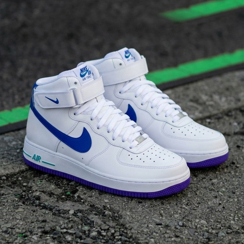 A pair of Nike Air Force 1 Mid sneakers in white, featuring a vibrant blue Swoosh and a purple outsole, resting on an asphalt surface with green painted lines.